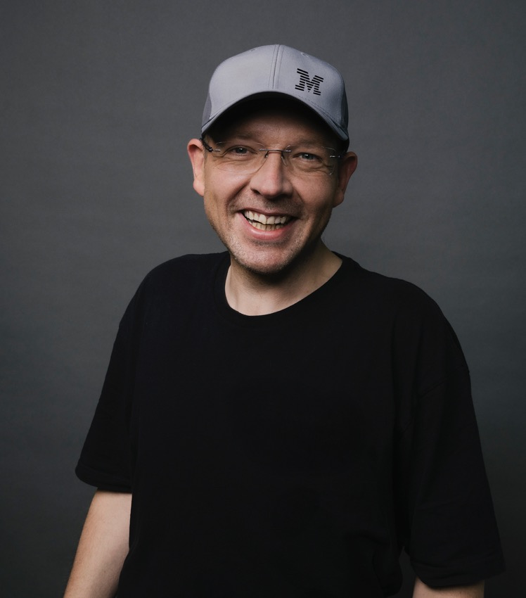 Markus Eisele smiling, wearing glasses and a gray cap